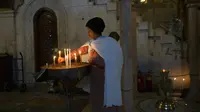 Seorang wanita menyalakan lilin dengan bayinya di punggung saat misa Kamis Putih di Kota Tua Yerusalem, Kamis (1/4/2021). Kamis Putih adalah hari Kamis sebelum Paskah dimana umat Kristen memiliki tradisi memperingati Perjamuan Malam terakhir yang dipimpin Yesus. (AP Photo/Maya Alleruzzo)