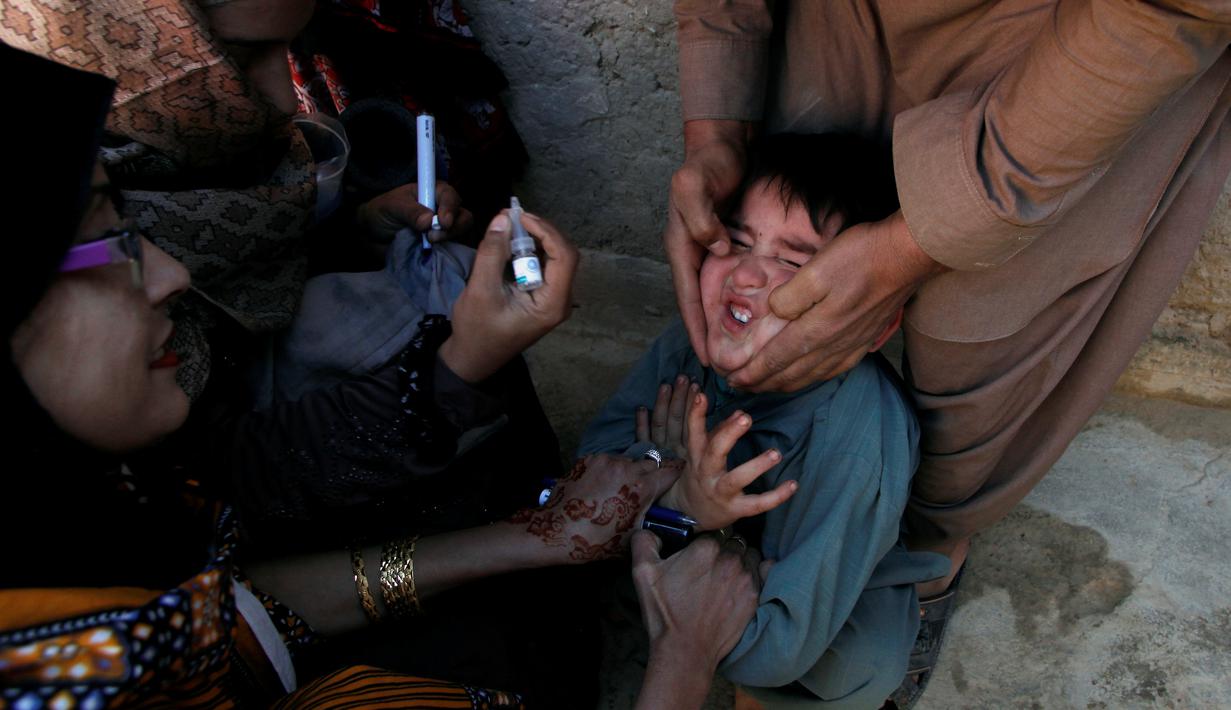 Seorang anak dipegangi orang tuanya saat petugas memberikan imunisasi polio di sepanjang jalan di Quetta, Pakistan, Senin (2/1). (REUTERS/Naseer Ahmed)