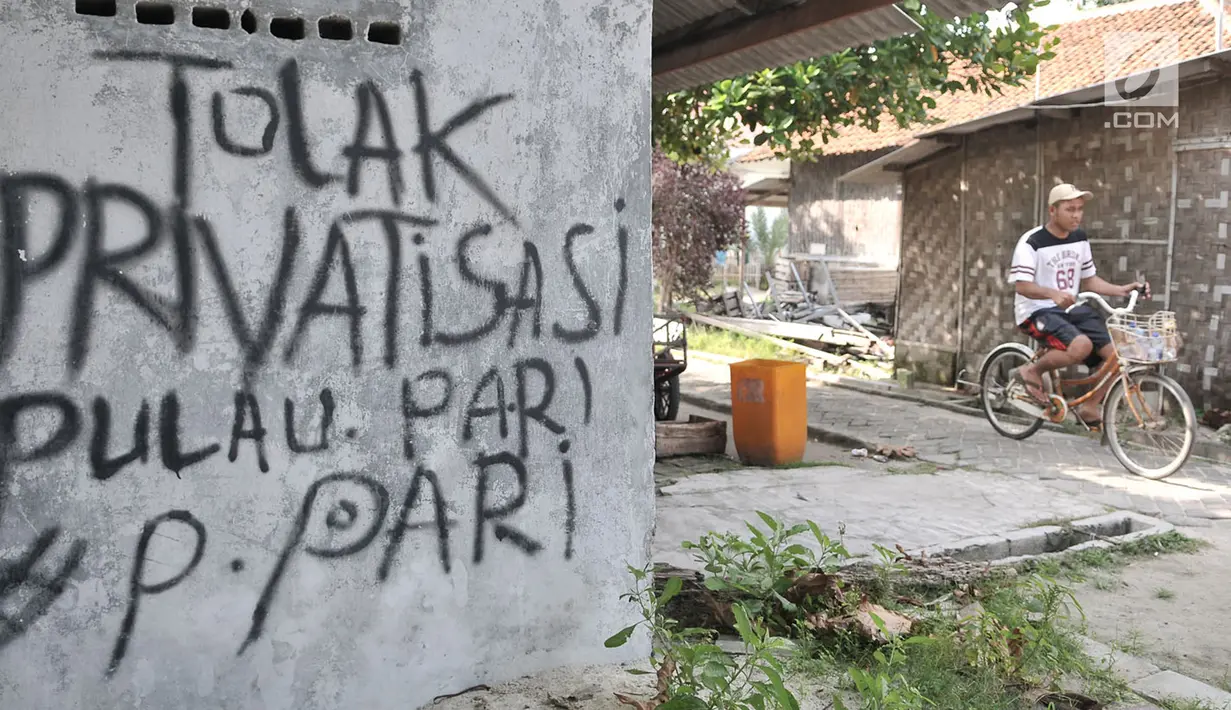 Wisatawan bersepeda melintasi coretan protes di salah satu tembok rumah di Pulau Pari, Kepulauan Seribu, Jakarta, Minggu (29/4). Coretan dibuat warga yang menolak klaim PT Bumi Pari Asri atas kepemilikan lahan Pulau Pari. (Merdeka.com/Iqbal S. Nugroho)