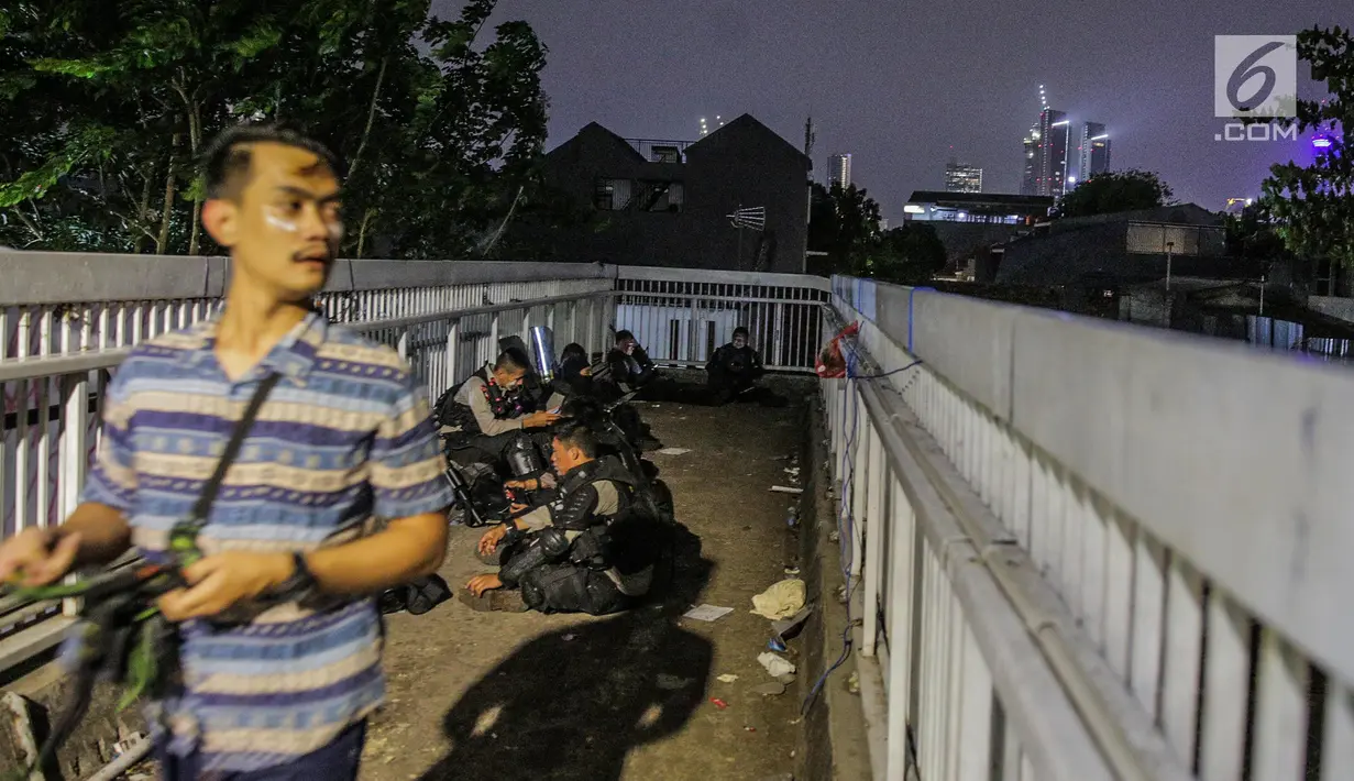 Aparat kepolisan melepas lelah di jembatan penyeberangan orang (JPO) depan Gedung DPR, Jakarta, Selasa (24/9/2019). Mereka melepas lelah usai mengawal demonstrasi mahasiswa menolak pengesahan RUU KUHP dan revisi UU KPK. (Liputan6.com/Faizal Fanani)