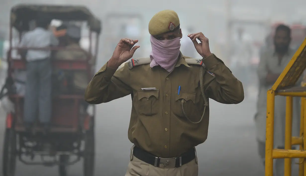 Polisi India menutup wajahnya dengan saputangan saat melewati jalan di New Delhi yang diselimuti kabut asap akibat polusi udara, Rabu (8/11). Organisasi Kesehatan Dunia menempatkan New Delhi sebagai kota paling berpolusi di dunia. (SAJJAD HUSSAIN/AFP)
