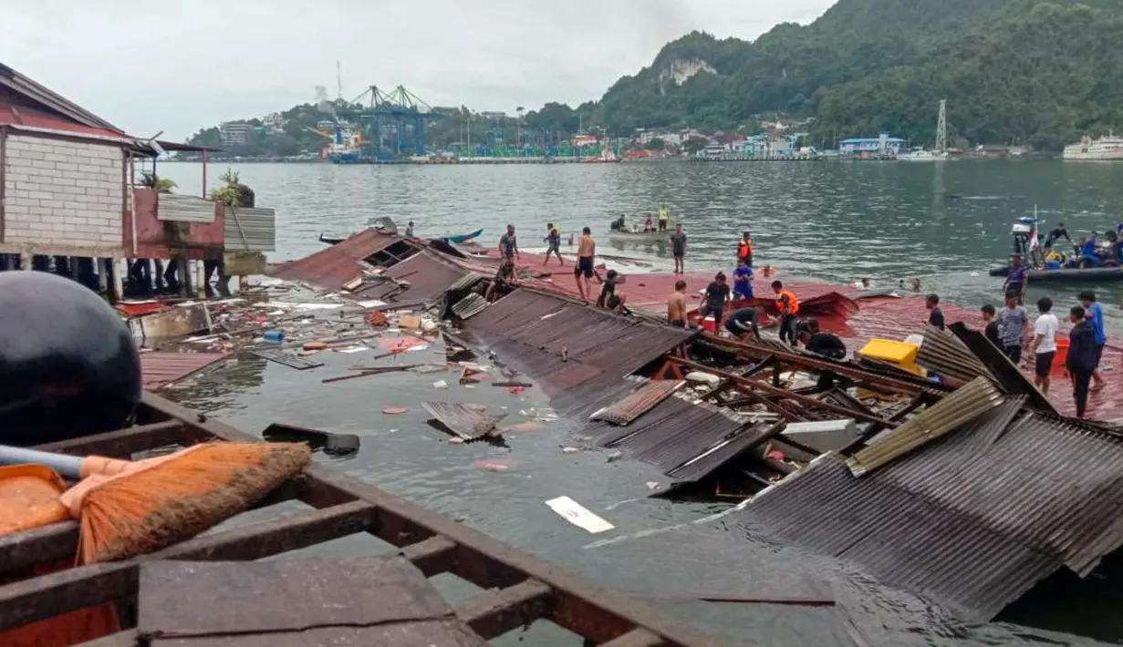 Orang-orang berdiri pada atap toko yang runtuh di pelabuhan setelah gempa magnitudo 5,1 di Jayapura, Provinsi Papua, Indonesia, 9 Februari 2023. Korban meninggal dalam gempa Jayapura adalah Rista (25), Ani (26), Astrid (25), dan Maya (27). (FAISAL NARWAWAN/AFP)