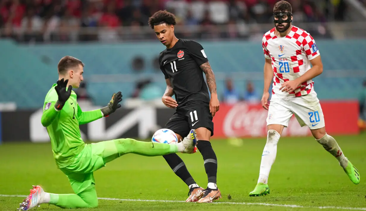 Kiper Kroasia Dominik Livakovic (1) melakukan penyelamatan melawan pemain Kanada Tajon Buchanan (11) saat bek Kroasia Josko Gvardiol (20) melihatnya pada pertandingan sepak bola Grup F Piala Dunia 2022 di Stadion Internasional Khalifa, Al Rayyan, Qatar, 27 November 2022. Kroasia mengalahkan Kanada dengan skor 4-1. (Nathan Denette/The Canadian Press via AP)