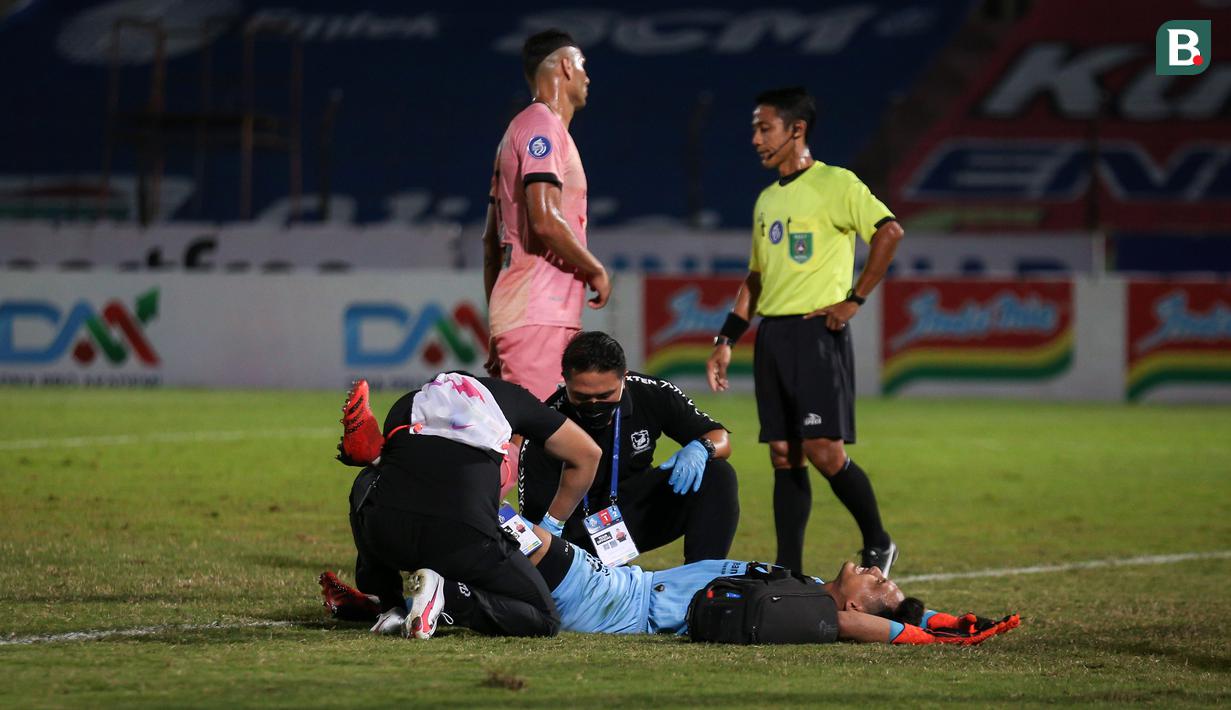 Ekspresi kesakitan kiper Madura United FC, Muhammad Ridho saat mendapat perawatan tim medis saat menghadapi Bali United dalam laga pekan ke-16 BRI Liga 1 2021/2022 di Stadion Sultan Agung, Bantul, Kamis (09/12/2021). (Bola.com/Bagaskara Lazuardi)