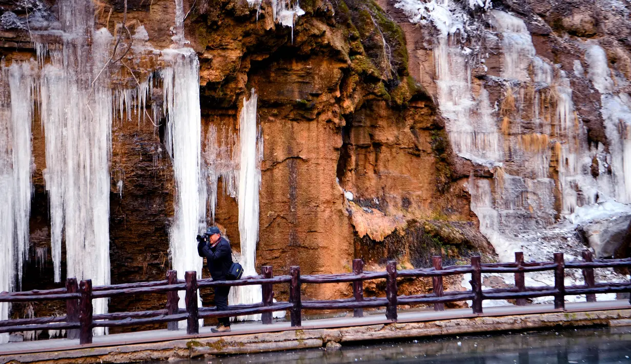 Seorang pengunjung memotret air terjun beku di objek wisata Gunung Yuntai di Jiaozuo, Provinsi Henan, China tengah, pada 24 Desember 2020. (Xinhua/Hao Yuan)
