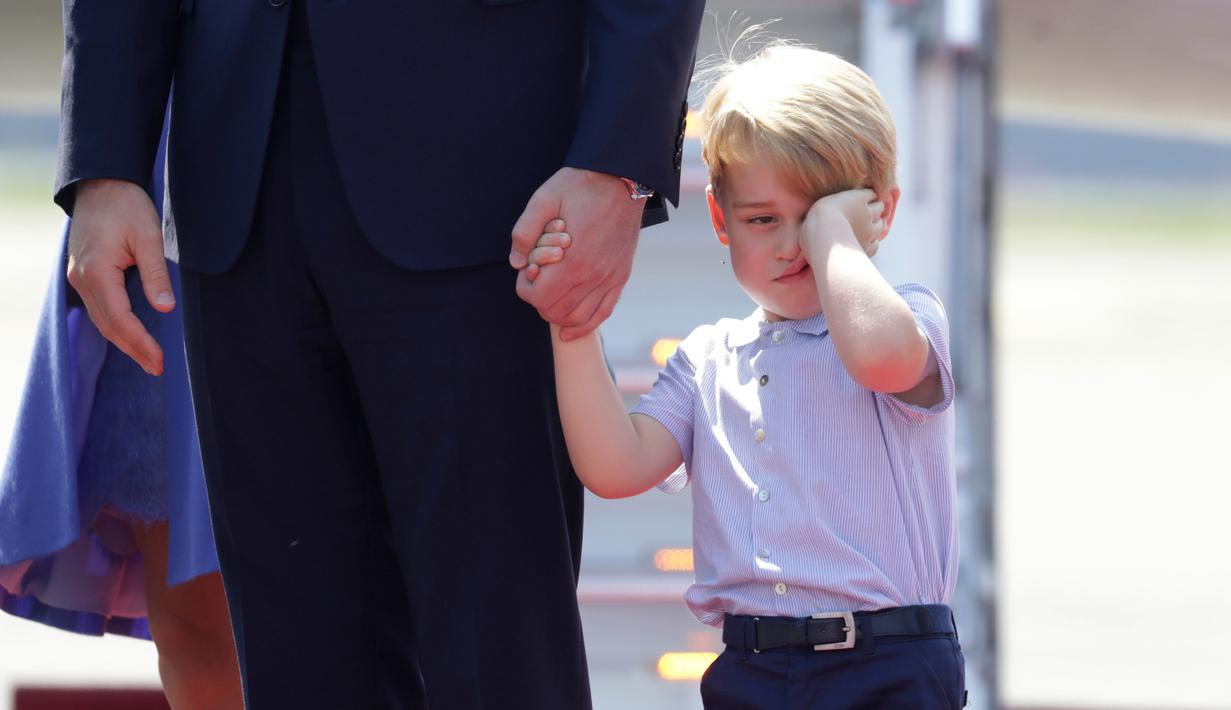 Pangeran George mengusap matanya sambil menggenggam tangan sang ayah, Pangeran William setibanya di Bandara Tegel, Berlin, Rabu (19/7). George ikut dalam tur keluarga kerajaan Inggris bersama Pangeran William dan Kate Middleton. (Kay Nietfeld/dpa via AP)