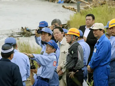 PM Shinzo Abe mendengarkan penjelasan petugas saat mengunjungi wilayah barat daya Jepang yang hancur akibat longsor dan banjir, Rabu (12/7). Abe berjanji pemerintah akan membantu pembangunan kembali di daerah itu segera. (Nozomi Endo/Kyodo News via AP)