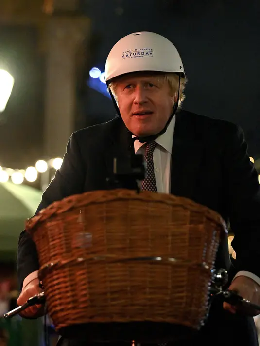 Perdana Menteri Inggris Boris Johnson mengendarai sepeda saat kunjungannya ke pasar Makanan dan Minuman Inggris yang didirikan di Downing Street, London, 30 November 2021. Sebanyak 12 bisnis dari seluruh Inggris memiliki kios untuk memamerkan produk mereka. (JUSTIN TALLIS/AFP/POOL)
