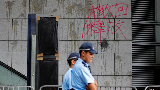 Polisi berjaga-jaga di depan tembok bertulis kata-kata China 'Penarikan dan Pembebasan' di pintu masuk utama kantor polisi di Hong Kong, Sabtu (22/6/2019). Markas polisi tersebut jadi korban aksi vandalime demonstran dalam lanjutan aksi unjuk rasa menolak RUU Ekstradisi. (AP Photo/Vincent Yu)