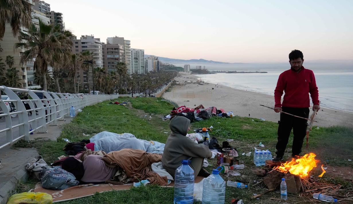 Hingga Jumat 6 Maret 2026, setidaknya ada 26 serangan udara Israel menghantam infrastruktur yang diklaim sebagai milik Hizbullah di Dahiyeh, pinggiran selatan Beirut. Tampak dalam foto, seorang pria pengungsi bersama keluarganya yang melarikan diri dari serangan udara Israel di Dahiyeh, pinggiran selatan Beirut, menyalakan api untuk menghangatkan diri di tepi pantai Beirut, Lebanon, Jumat 6 Maret 2026. (AP Photo/Hussein Malla)