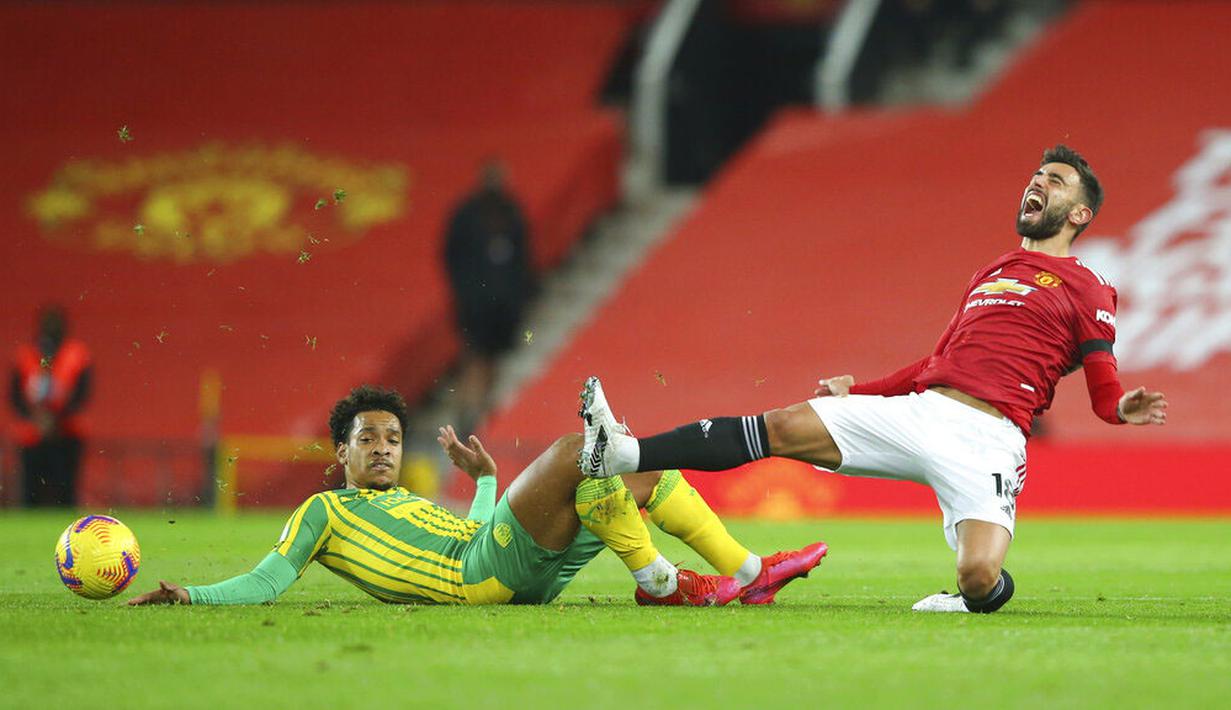 Gelandang Manchester United, Bruno Fernandes, meringis kesakitan saat berebut bola dengan pemain West Bromwich Albion, Matheus Pereira, pada laga Liga Inggris di Stadion Old Trafford, Minggu (22/11/2020). MU menang dengan skor 1-0. (Alex Livesey/Pool via AP)