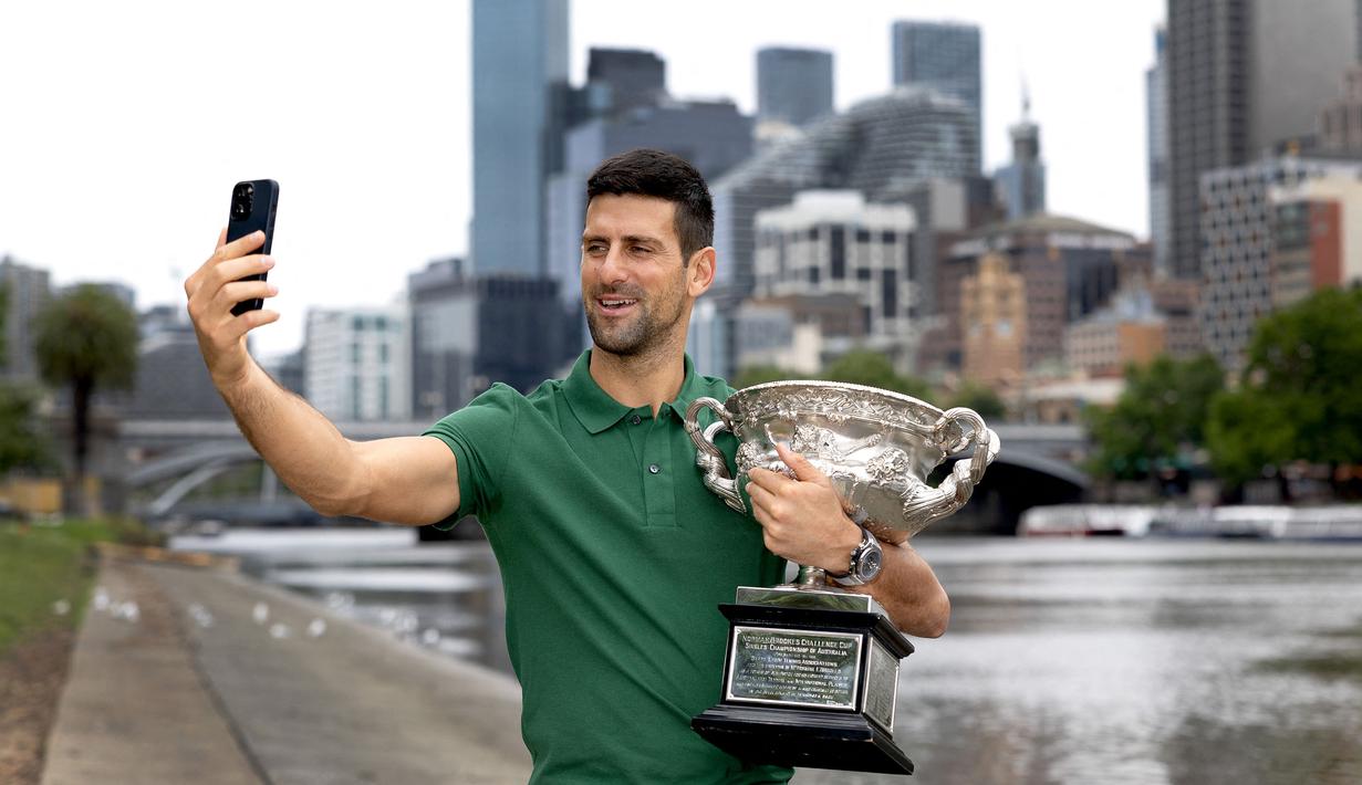 Petenis tunggal putra Serbia, Novak Djokovic melakukan swafoto bersama trofi Norman Brooks Challenge Cup setelah menjadi juara pada Australia Open 2023 di dekat sungai Yarra, Melbourne, Australia, Senin (30/01/2023). Djokovic berhasil mengalahkan petenis Yunani, Stefanos Tsitsipas di babak final dengan skor 6-3, 7-6(7-4), 7-6(7-5). (AFP/Fiona Hamilton)