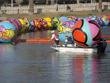 Relawan mengunakan perahu bersiap menurunkan bola raksasa ke danau MacArthur Park selama pameran "Spheres" di Los Angeles, California, AS (21/8/2015). Acara ini menampilkan sekitar 3.000 bola raksasa yang dihias oleh para relawan. (REUTERS/Mario Anzuoni)