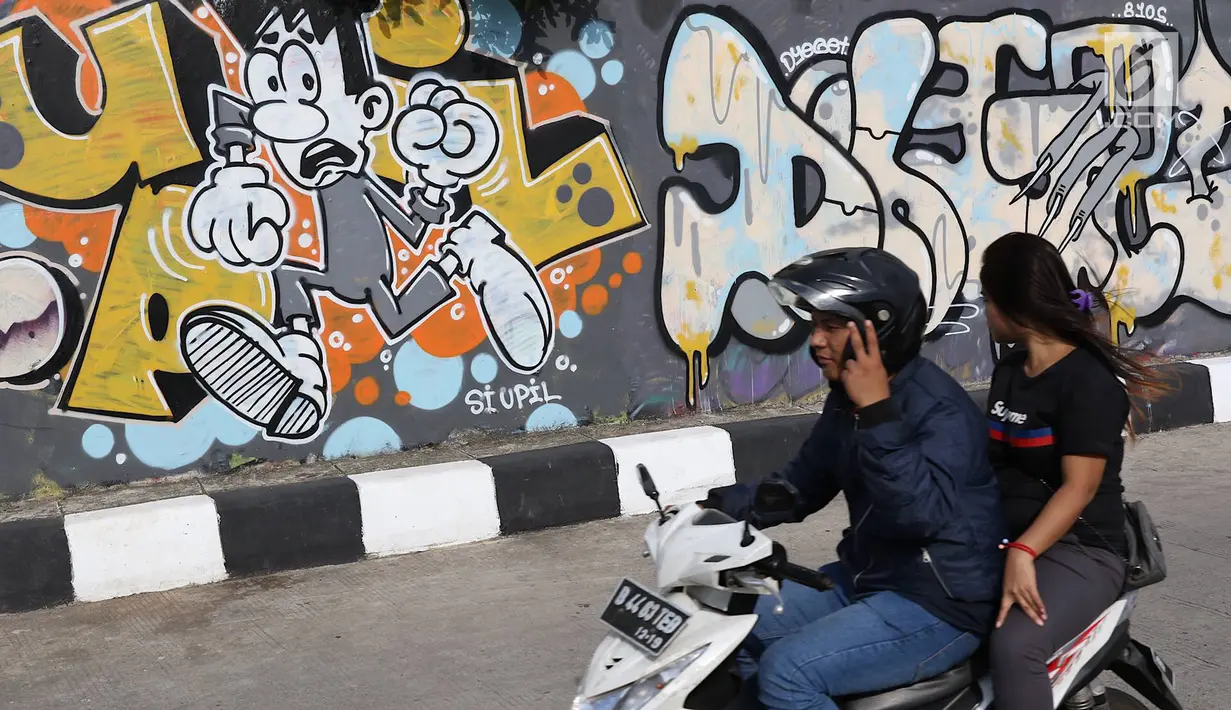 Pengendara melintasi jalur inspeksi Sungai Ciliwung di Jakarta, Kamis (27/12). Mural yang dibuat oleh beberapa komunitas tersebut menjadikan jalur inspeksi Sungai Ciliwung tampak lebih berwarna dan asri. (Liputan6.com/Immanuel Antonius)