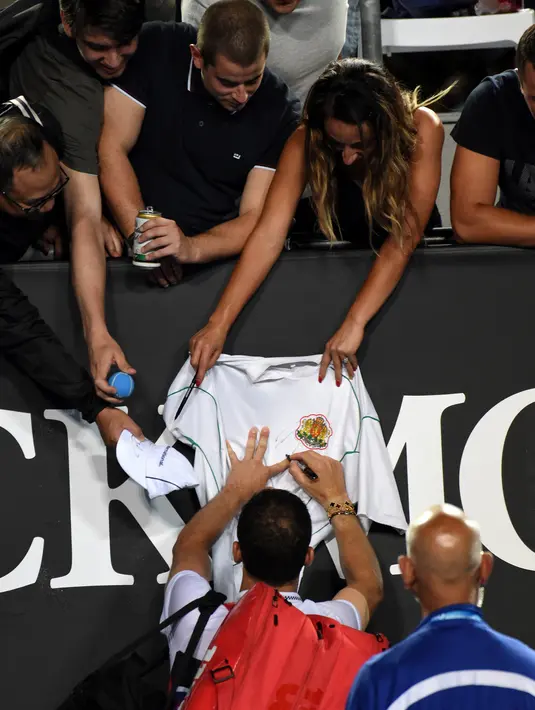 Petenis Bulgaria, Grigor Dimitrov menandatangi jersey yang disodorkan penggemarnya setelah menang atas Pablo Cuevas dari Uruguay pada pertandingan tunggal putra turnamen Australia Terbuka di Melbourne, Rabu (16/1). (Photo by Greg Wood / AFP)