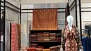 Set busana yang terbuat dari kain songket bernuansa coklat tua dengan motif geometris dan floral berwarna emas yang berpola berulang. Potongan bajunya berupa gaun panjang berkerah V yang menyatu dengan rok lurus, memberikan kesan anggun dan ramping. Lengan panjang berbahan sama digunakan sebagai outer atau selendang, menambah sentuhan elegan serta mempertegas karakter mewah khas songket tradisional. (Foto: instagram@/zainalsongket)