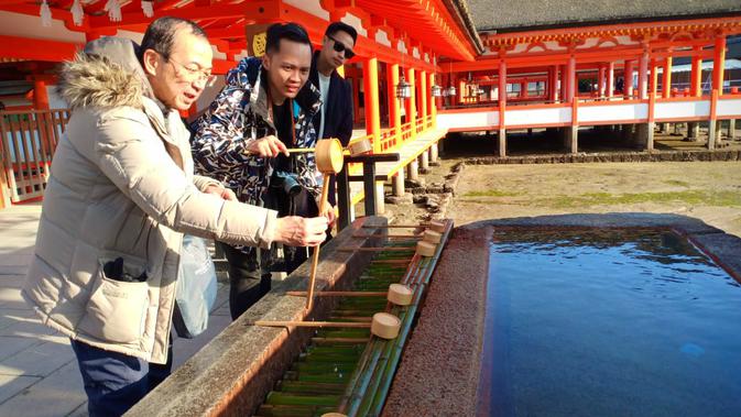 Pemandu tur Fumio Ito sedang memperagakan cara mencuci tangan di Kuil Itsukushima (Liputan6.com/ Mevi Linawati)