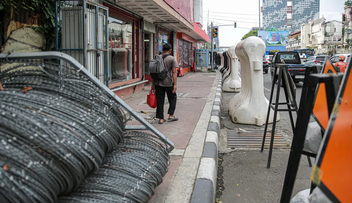 Warga berjalan kaki di samping barrier atau penghalang di kawasan Harmoni, Jakarta, Kamis (27/10/2022). Barrier yang biasa digunakan ketika terjadi demonstrasi Itu menyulitkan pejalan kaki saat melintas di trotoar. (Liputan6.com/Faizal Fanani)