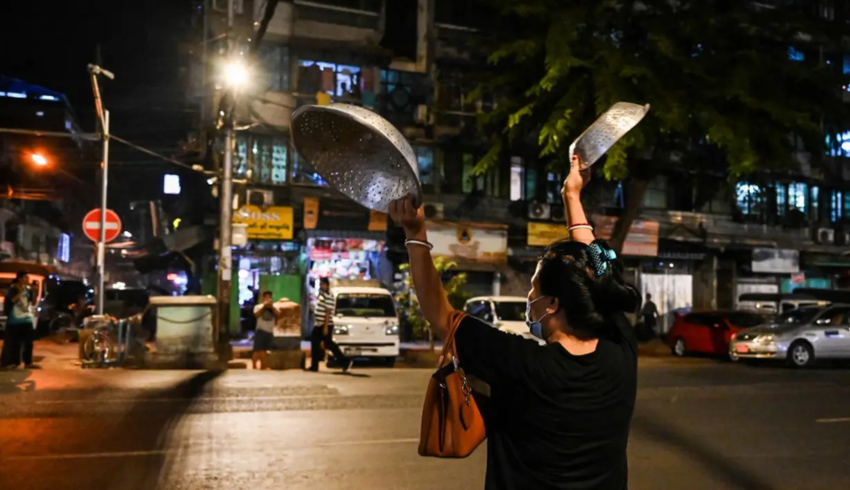 Seorang wanita membuat keributan dengan memukul-mukul panci setelah seruan untuk protes keluar di media sosial di Yangon, Myanmar, 3 Februari 2021. Kudeta militer Myanmar terus memicu protes warga dengan membunyikan klakson mobil, menyalakan lampu ponsel, dan memukul-mukul panci. (STR/AFP)