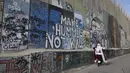 Seorang pria mengenakan pakaian Sinterklas berjalan di sepanjang tembok pemisah Israel di kota Bethlehem, Tepi Barat yang alkitabiah pada 22 Desember 2022, menjelang Natal. (AFP/Hazem Bader)