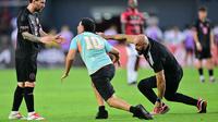 Pengawal Lionel Messi, Yassine Cheuko (kanan) berusaha bangkit setelah terjatuh saat menangkap seorang penyusup lapangan dalam laga persahabatan antara Inter Miami melawan Sporting San Miguelito di Stadion Romeo Fernandez, Panama, Amerika, Senin (03/02/2025) waktu setempat. (AFP/Martin Bernetti)