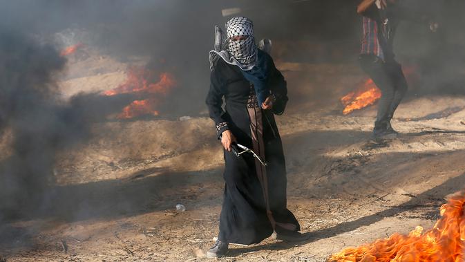 Pengunjuk rasa wanita Palestina memegang ketapel di tengah asap hitam saat terjadi bentrok antara warga dengan tentara Israel di Khan Younis, perbatasan Gaza, Jumat (10/8). (AP Photo/Adel Hana)