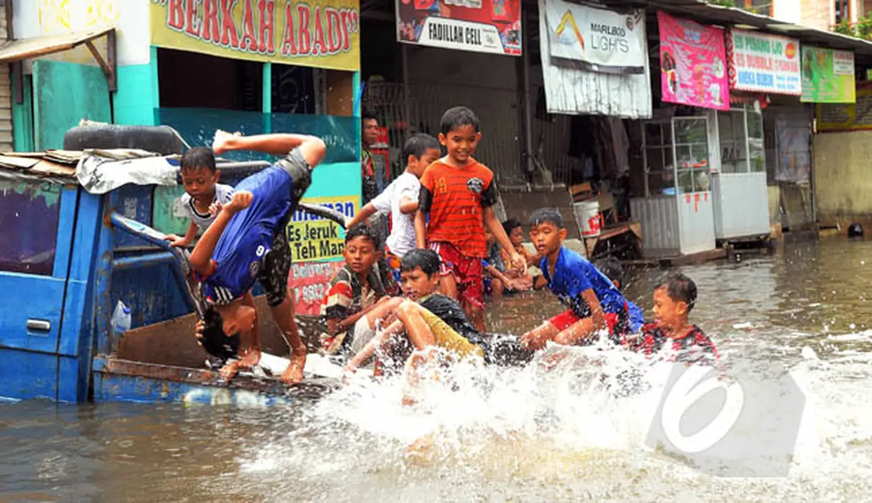 Sejumlah anak-anak asyik bermain di atas sebuah mobil yang terendam banjir di kawasan Grogol, Jakarta Barat, Rabu (11/2/2015). (Liputan6.com/Faisal R Syam)