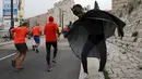 Seorang pria mengenakan kostum superhero Batman menggoda para atlet lari di kota tua, Yerusalem, Israel, (18/2).  Sejumlah orang mengikuti lomba lari Maraton Internasional  yang ke-6 di Yerusalem. (REUTERS / Baz Ratner)