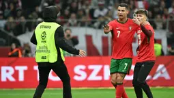 Pemain Portugal, Cristiano Ronaldo (tengah) menahan pihak keamanan yang akan menangkap seorang penyusup lapangan saat laga lanjutan EUFA Nations League Polandia di National Stadium, Warsawa, Polandia, Minggu (13/10/2024) WIB. (AFP/Sergei Gapon)