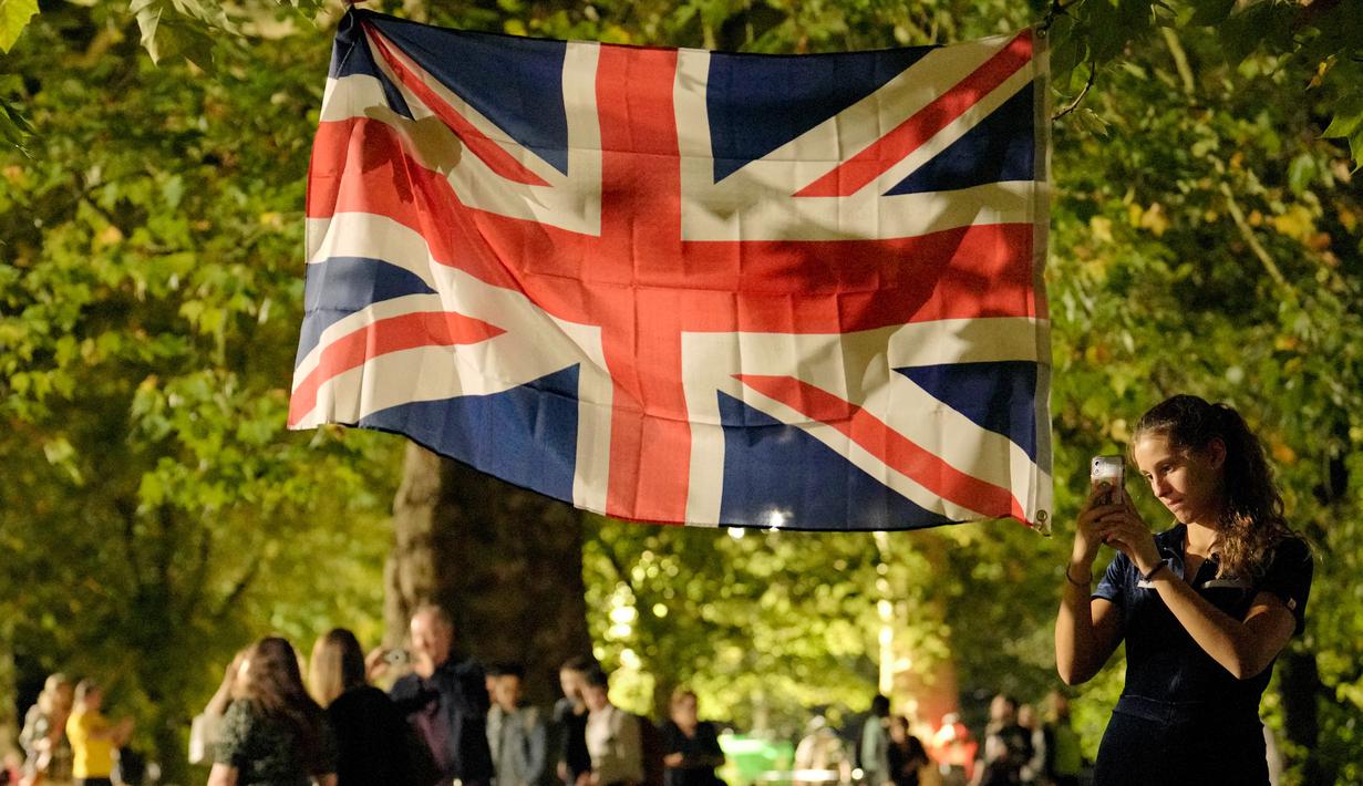 <p>Seorang wanita mengambil foto lambang bendera Inggris saat orang-orang memberikan penghormatan bunga kepada Ratu Elizabeth II di Green Park London, Senin, (12/6/2022). Bukan hanya itu, Ratu Inggris ini juga menjadi pimpinan semua cabang militer Inggris dan menjadi pendukung keuangan atas lebih dari 700 organisasi di seluruh dunia. (AP Photo/Vadim Ghirda)</p>