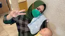Kali ini, berpose setelah berhasil menidurkan sang cucu Rayyanza, Rieta Amilia menunjukkan dua jarinya dengan outfit kemeja flanel bernuansa hijau, yang dipadunya dengan jilbab segiempat yang juga berwarna hijau. Foto: Instagram.