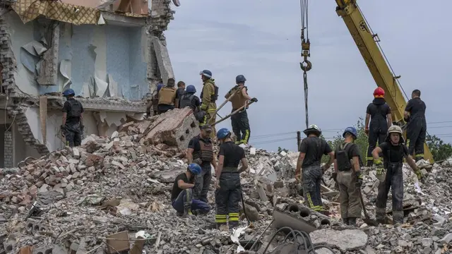Petugas penyelamat berdiri di atas puing-puing di tempat kejadian setelah serangan rudal Rusia mengenai blok apartemen perumahan, di Chasiv Yar, wilayah Donetsk, Ukraina timur, Minggu, 10 Juli 2022. (AP Photo/Nariman El-Mofty)