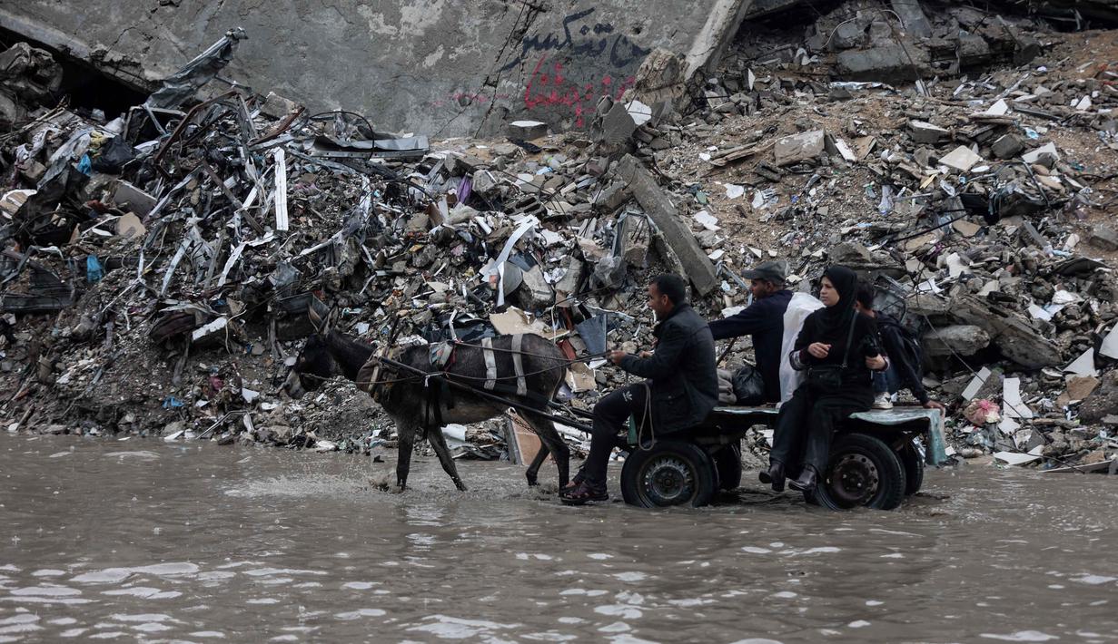 Data Kementerian Kesehatan di Gaza yang dikelola Hamas menyebut, hingga Rabu 26 November 2025, serangan Israel di Gaza telah menewaskan sedikitnya 69.775 orang. Tampak dalam foto, orang-orang menunggangi kereta kuda melewati banjir di kamp darurat yang menampung warga Palestina yang terlantar setelah hujan deras di Kota Gaza pada Selasa 25 November 2025. (Omar AL-QATTAA/AFP)