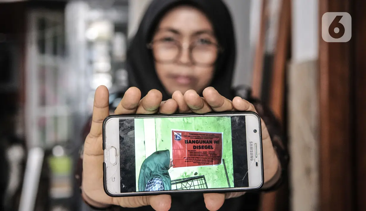 Wiwiek (56) menunjukkan foto saat proyek pembangunan gedung sekolah Pergunas I disegel di Jalan Cempaka Baru I, RT 015/003, Kemayoran, Jakarta, Senin (31/8/2020). Pembangunan itu menutup akses jalur keluar masuk dan harus melewati pintu samping. (merdeka.com/Iqbal S Nugroho)