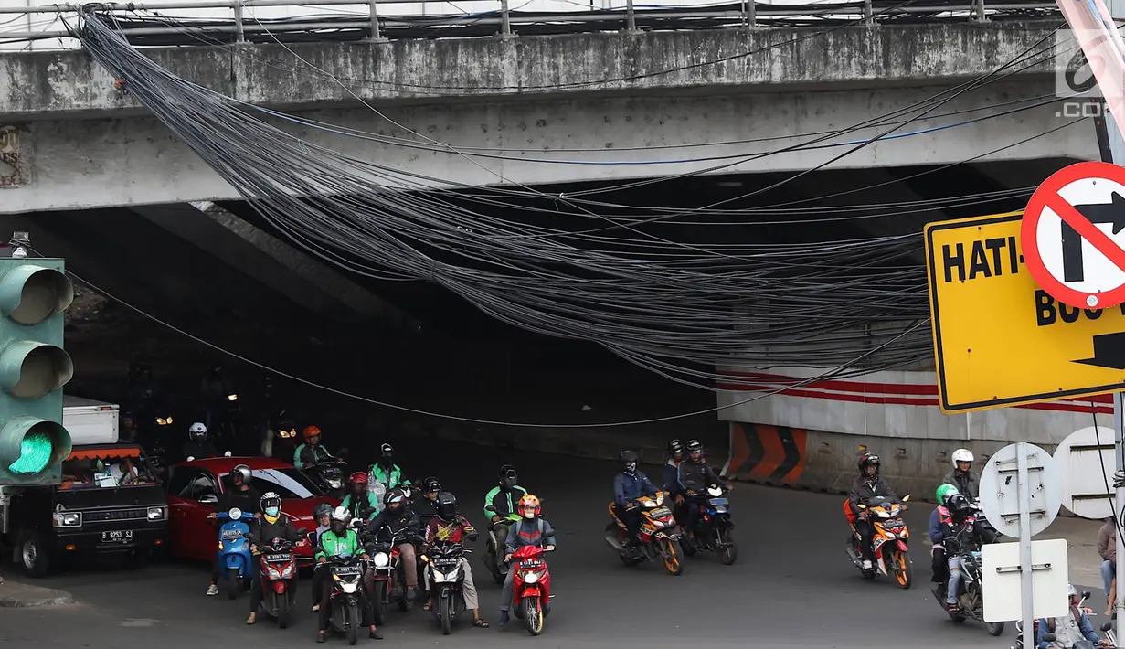 Kendaraan melintas di bawah Instalasi kabel menjuntai di Jalan Dewi Sartika, Jakarta Timur, Sabtu (19/1). Selain mengganggu keindahan kota, kondisi tersebut juga berbahaya karena dapat memicu hubungan pendek arus listrik. (Liputan6.com/Immanuel Antonius)