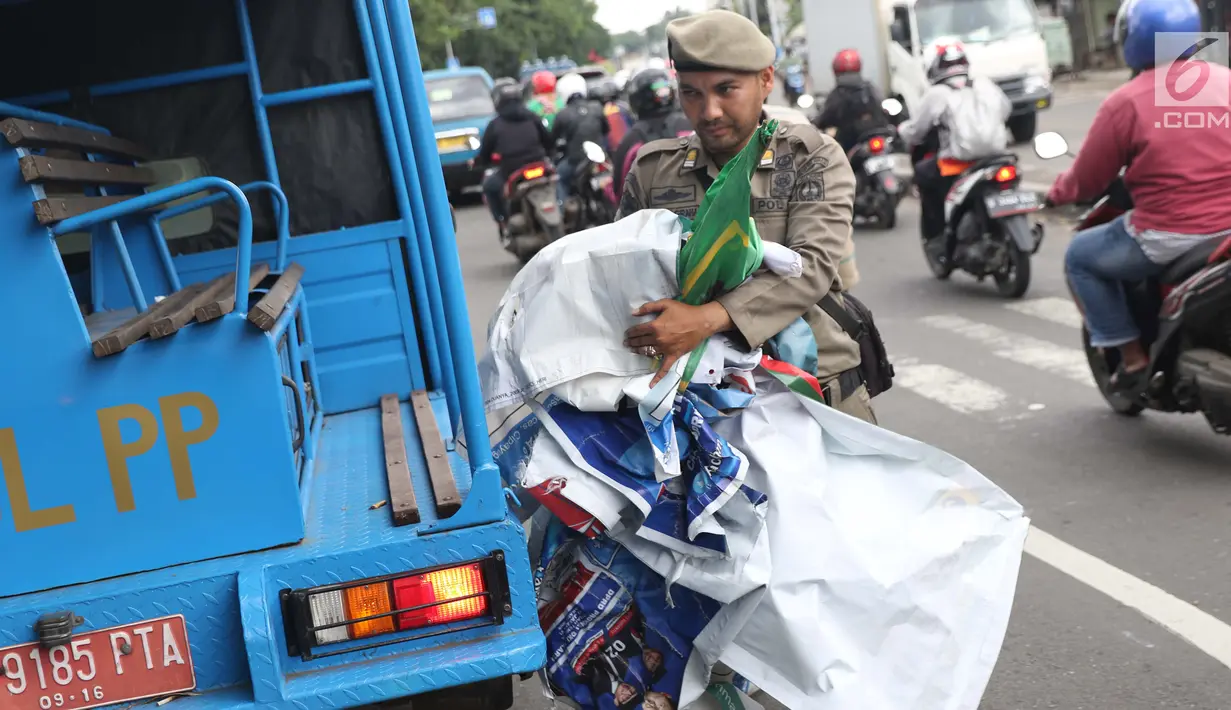 Petugas Satpol PP membawa APK usai diturunkan dari pagar pembatas di Jalan Raya Bogor dekat GOR Ciracas, Jakarta, Rabu (23/1). Penurunan APK ini karena pemasangannya dianggap melanggar ketentuan. (Liputan6.com/Helmi Fithriansyah)