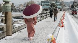 Pejalan kaki melintasi jembatan yang tertutup salju di atas Sungai Kamo setelah salju tebal dan angin kencang semalaman mempengaruhi wilayah luas negara itu di Kyoto, Jepang, Rabu (25/1/2023). Sejumlah area yang luas di Jepang, termasuk di sisi Pasifik, dapat mengalami hujan salju lebat dari Selasa malam 24 Januari 2023 hingga Rabu 25 Januari 2023. (Fred Mery / AFP)