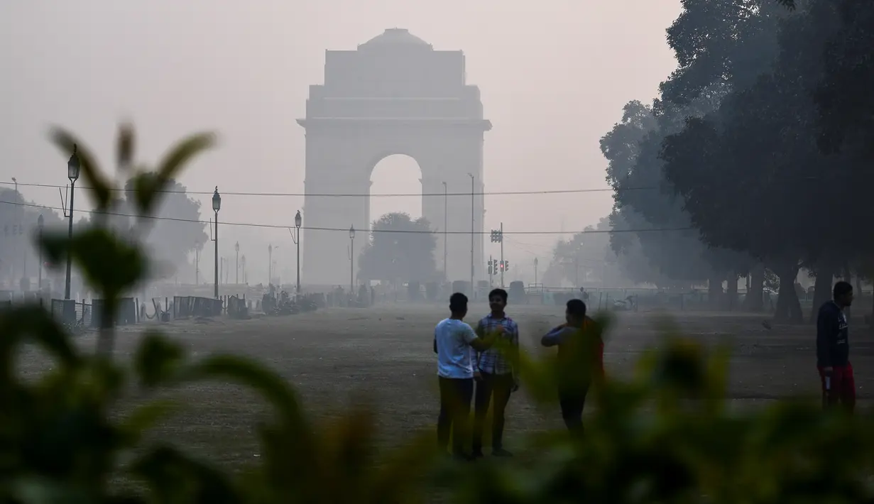 Orang-orang mengobrol sambil berdiri di taman dekat Gerbang India di tengah kondisi asap tebal yang menyelimuti sehari setelah perayaan Diwali, festival cahaya Hindu, di New Delhi pada Minggu (15/11/2020). (Photo by Sajjad HUSSAIN / AFP)