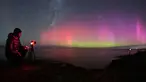 Seorang pria memotret Aurora Australis saat bersinar di cakrawala di atas perairan Danau Ellesmere di pinggiran Christchurch, Selandia Baru pada 24 April 2023. (AFP/Sanka Vidanagama)