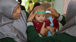 Seorang tenaga kesehatan mengukur lingkar kepala bayi selama program imunisasi massal di Surabaya pada 15 September 2025. (Juni KRISWANTO/AFP)