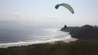 Seorang atlet paralayang terbang melayang di atas Pantai Modangan. Salah satu pantai di Malang ini jadi spot terbaik berlatih paralayang (Pemdes Sumberoto)