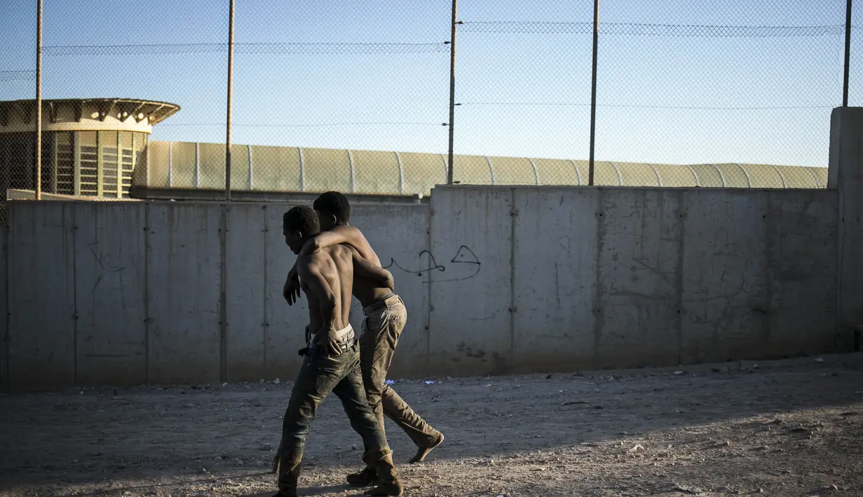 Seorang migran membantu yang lain berjalan setelah melintasi pagar yang memisahkan daerah kantong Spanyol Melilla dari Maroko, di Melilla, Spanyol (3/3/2022). Ratusan orang Afrika telah mencoba memanjat pagar yang memisahkan kota Melilla di Spanyol dari Maroko. (AP Photo/Javier Bernardo)