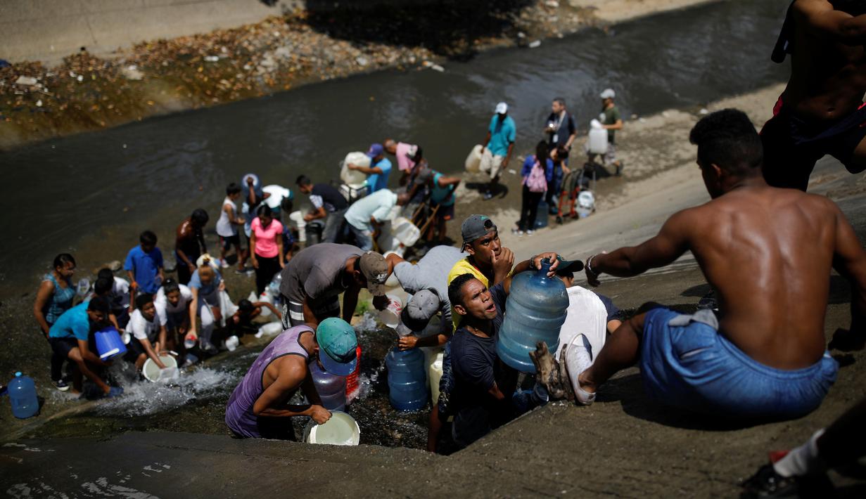 Orang-orang mengumpulkan air yang keluar melalui saluran pembuangan air limbah yang mengalir ke Sungai Guaire di Caracas, 11 Maret 2019. Pemadaman listrik selama berhari-hari di Venezuela berdampak terhadap krisis air. (REUTERS/Carlos Garcia Rawlins)