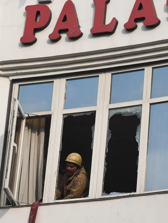 Petugas pemadam kebakaran melihat keluar jendela yang rusak setelah kebakaran Hotel Arpit Palace di Distrik Karol Bagh, New Delhi, Selasa (12/2). Sejauh ini belum diketahui penyebab munculnya api yang memicu kebakaran tersebut. (Prakash SINGH / AFP)