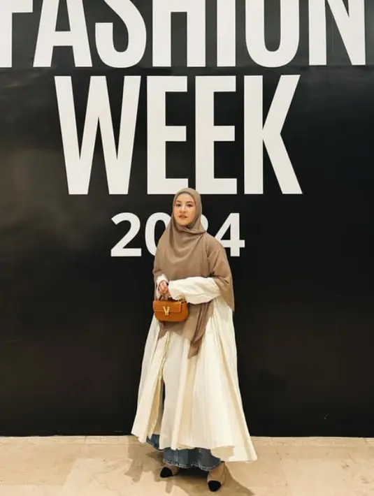 Natasha Rizky mengenakan dress loose putih dipadukan kerudung coklat tua serta rok denim dan flat shoes. Sambil membawa mini bag coklat. [@natasharizkynew]