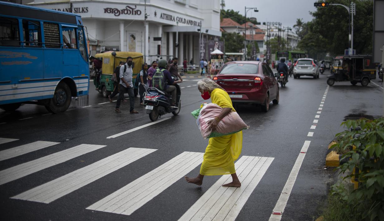 Seorang wanita tua yang mengenakan masker berjalan tanpa alas kaki melalui zebra cross di Kochi, negara bagian Kerala, India, Rabu (6/7/2022). Negara bagian selatan itu telah mewajibkan penggunaan masker di tempat-tempat umum menyusul meningkatnya kasus COVID-19. (AP Photo/ RS Iyer)