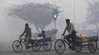 Pria India mengayuh becak roda tiga membawa air minum di tengah kabut tebal di New Delhi (25/12). India ditetapkan darurat polusi udara. Kualitas udara yang semakin buruk dan kabut beracun menyelimuti. (AFP Photo/Prakash Singh)