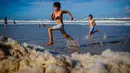 Anak-anak bermain di antara busa pantai setelah siklon tropis di Currumbin Beach, Gold Coast, Australia pada 15 Desember 2020. Hujan lebat dan angin kencang telah melanda kawasan perbatasan padat penduduk antara New South Wales dan Queensland selama tiga hari. (Photo by Patrick HAMILTON / AFP)