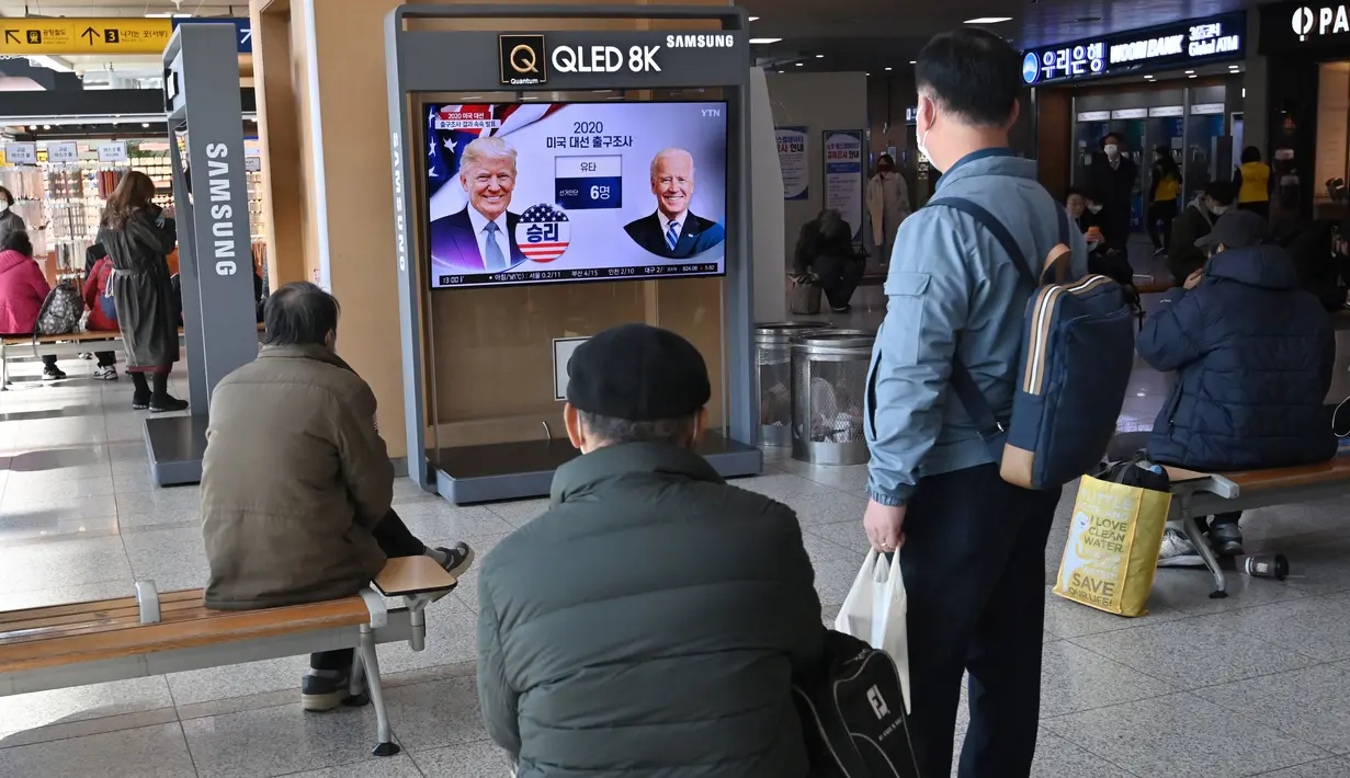 Orang-orang menonton program berita televisi tentang pemilihan presiden (pilpres) AS yang menampilkan gambar Presiden Donald Trump (kiri) dan calon presiden dari Partai Demokrat Joe Biden (kanan), di sebuah stasiun kereta api di Seoul, Korea Selatan pada Rabu (4/11/2020). (Photo by Jung Yeon-je / AF