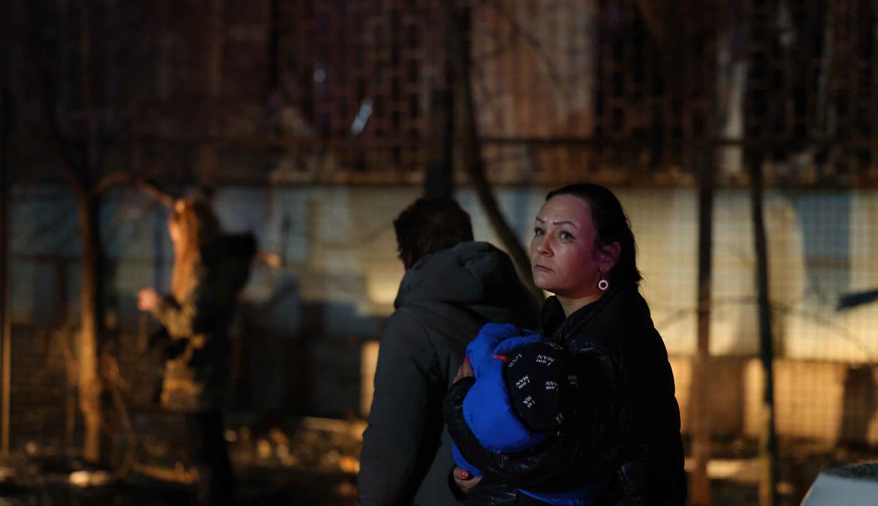 Sementara, Layanan Darurat Negara Ukraina menyampaikan bahwa kebakaran kini telah terkendali, sementara proses evakuasi dan pencarian korban tetap dilakukan. Tampak dalam foto, seorang perempuan menggendong anaknya di depan bangunan tempat tinggal yang terbakar setelah serangan Rusia di Zaporizhzhia, Ukraina, Rabu 26 November 2025. (AP Photo/Kateryna Klochko)